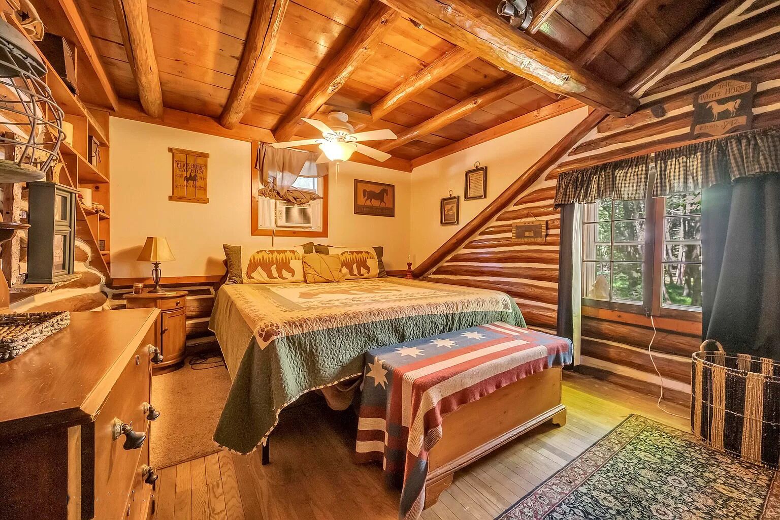 A cozy log cabin bedroom with a bed, a desk, and a window with curtains.