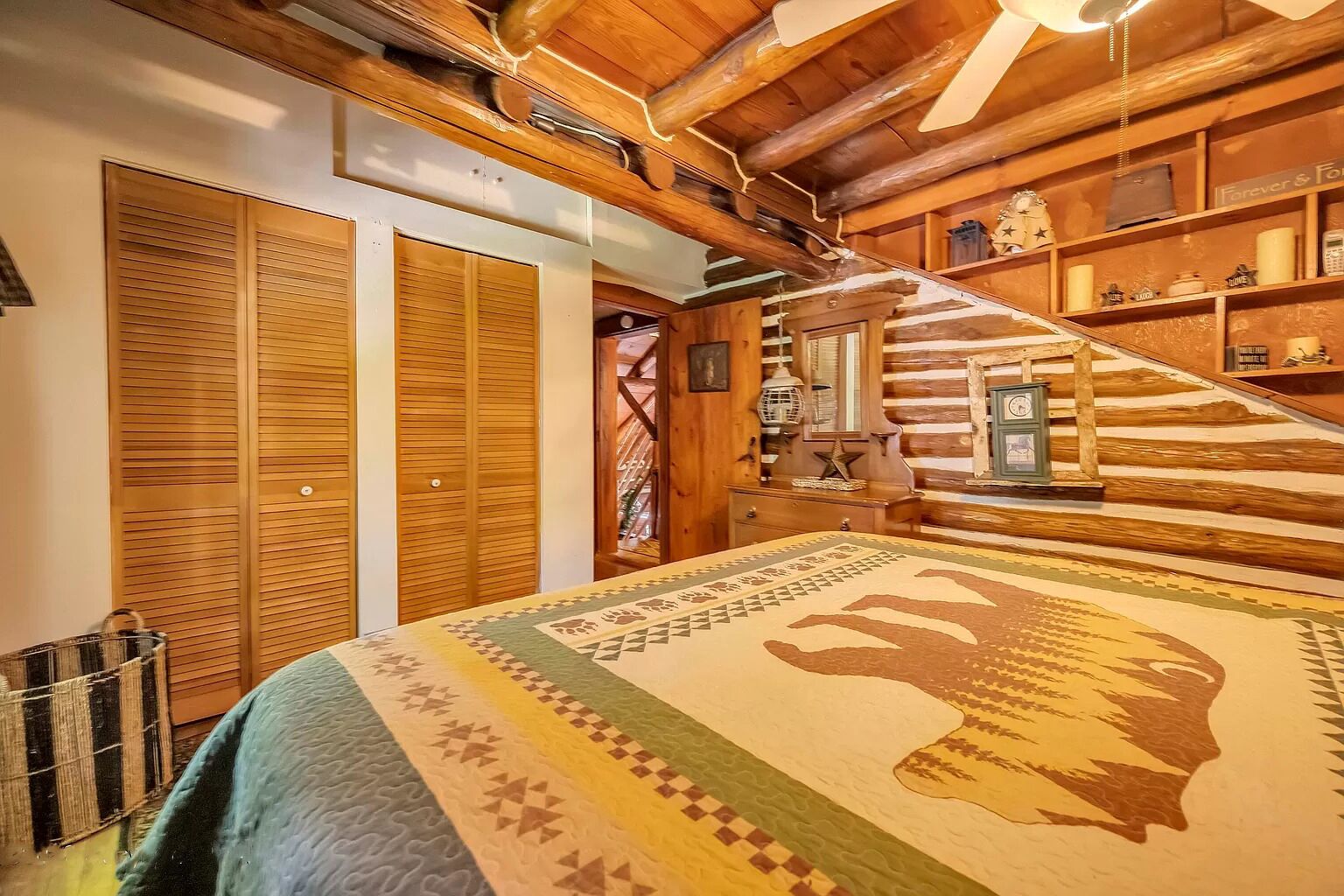 Un dormitorio de estilo cabaña de troncos con cama, armarios de madera, una escalera y estante con objetos decorativos.