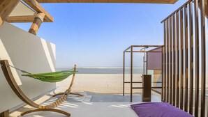 Ein Zimmer direkt am Strand mit einer Hängematte, einem violetten Kissen und Blick auf den Strand.