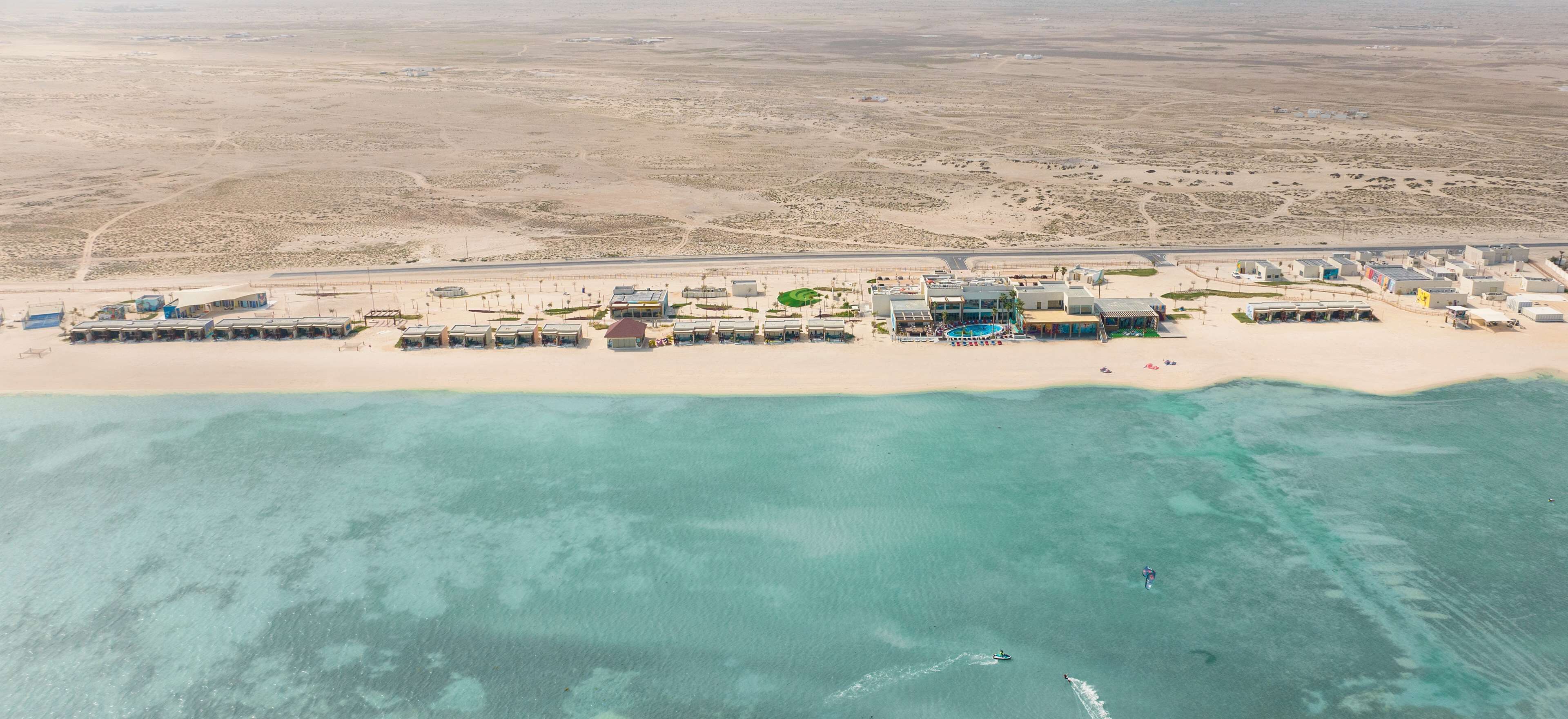 Vue aérienne d’un hôtel situé sur la côte, composé de plusieurs bâtiments, avec une plage et des eaux turquoise d’une clarté exceptionnelle.