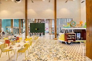 Un amplio comedor con techos altos y paredes de ladrillo visto, que presenta un camión de comida único y una pared verde con un diseño geométrico.