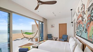 Ein Hotelzimmer mit einem großen Bett, einem Sessel, einem kleinen Tisch, einer Hängematte und Blick auf den Strand.