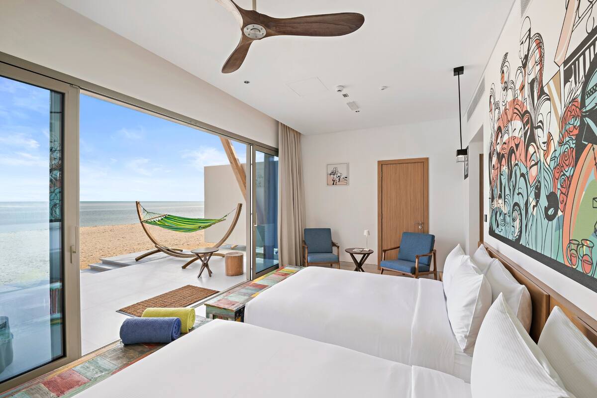 Une chambre d’hôtel avec un grand lit, une chaise, une petite table, un hamac et une vue sur la plage.