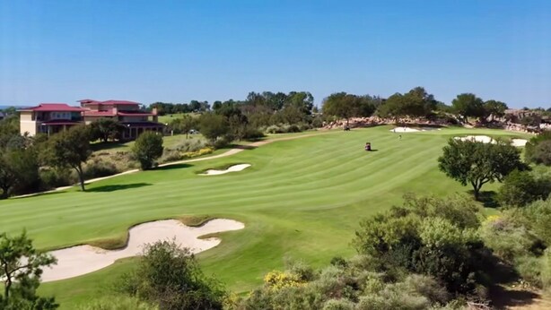 Un campo de golf con club house, búnkeres de arena y árboles.
