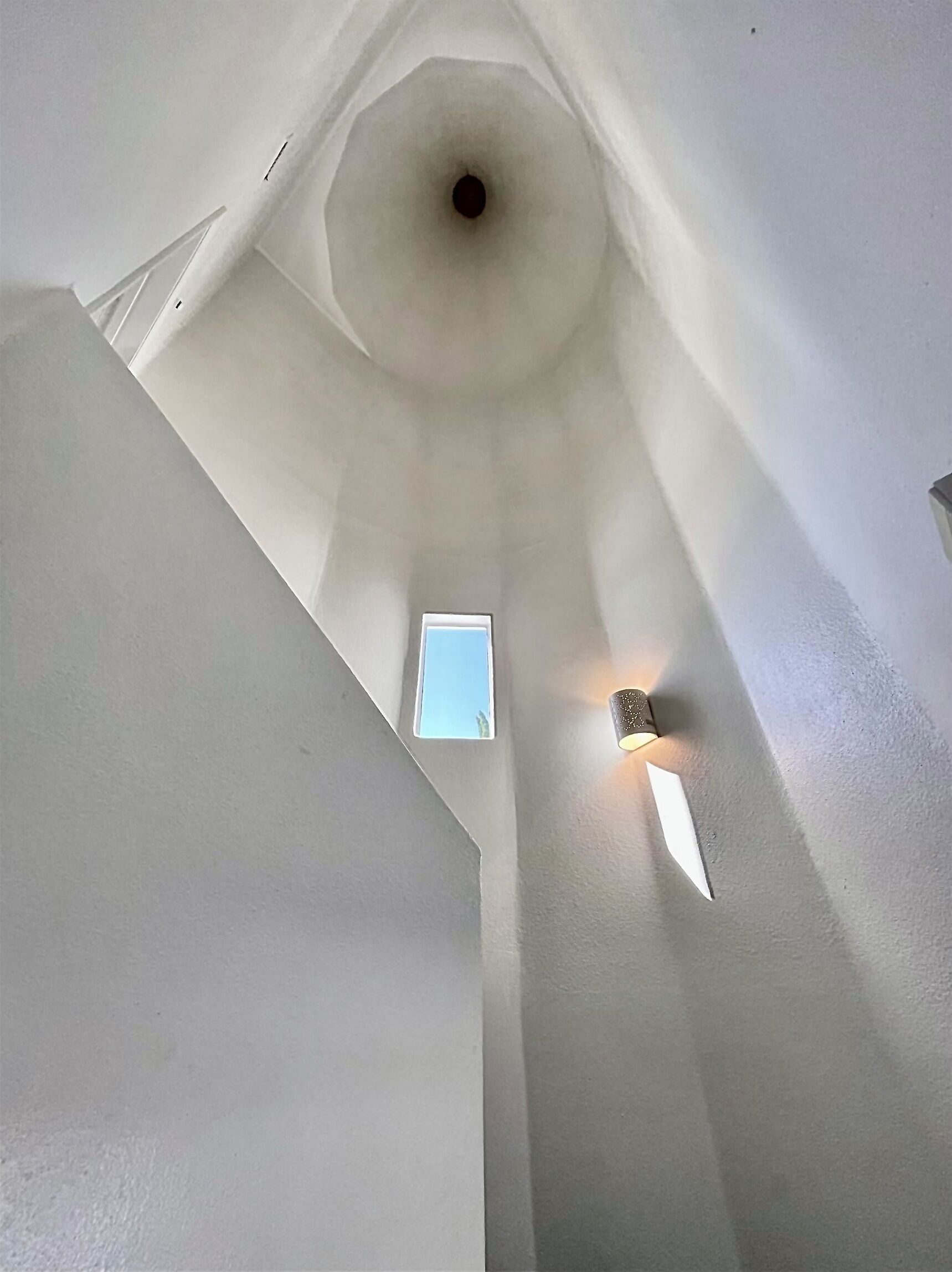 A high ceiling with a skylight and a small window, and a wall-mounted light fixture.