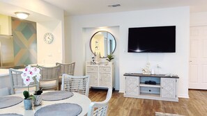A modern living room with a dining area, a flat-screen TV mounted on the wall, and a decorative mirror. - Gulf Terrace, Destin, Beautifully decorated . 5 Min. to Big Kahuna (Destin)