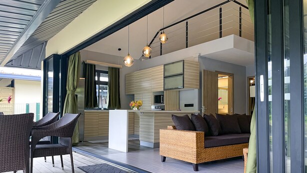 Un salon moderne avec un canapé, des fauteuils et un coin repas, la cuisine étant visible au fond.