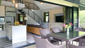 Un intérieur moderne avec un îlot central, des meubles en osier, un escalier et un grand téléviseur.