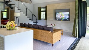 Un salon moderne avec un escalier, un téléviseur à écran plat et un canapé en osier.