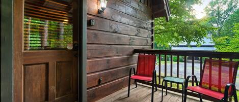A wooden porch with a door, two red chairs, and a small table.