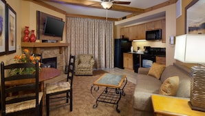 A cozy living room with a fireplace, a dining table with chairs, a sofa, and a television mounted on the wall.
