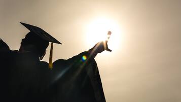 A silhouette of a person wearing a graduation cap against a bright light source.
