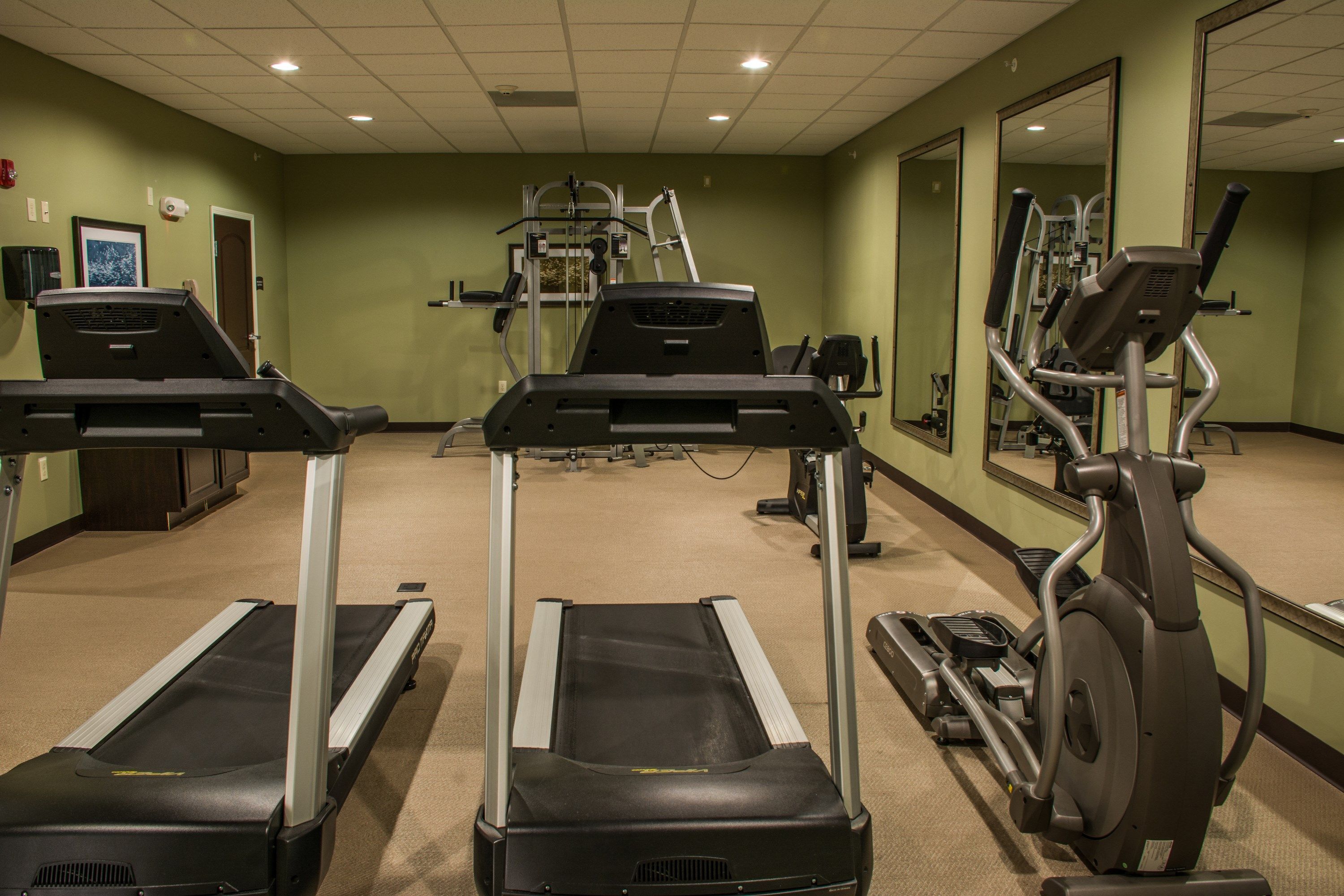 A gym with treadmills, an elliptical, and a mirror wall.