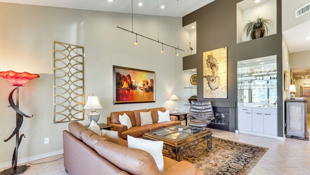 A spacious living room with a brown leather sofa, a glass coffee table, and a large abstract painting on the wall. - Patio + Resort Amenities: Palm Desert Escape (Palm Desert)