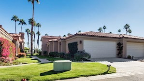 A residential house with a well-maintained lawn, a large air conditioning unit, and a garage. - Patio + Resort Amenities: Palm Desert Escape (Palm Desert)