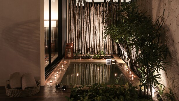 Un área de piscina interior tranquila con un fondo de bambú, velas y un pequeño farol.