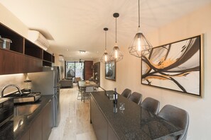 A modern kitchen with a central island, stainless steel appliances, pendant lighting, and a dining area with chairs and a table.