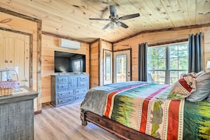 Ein Schlafzimmer einer Holzhütte mit Bett, Schminktisch, Fernseher und großen Fenstern.