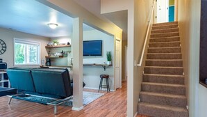 A spacious living area with a sofa, a TV mounted on the wall, and a staircase leading to another level.
