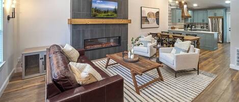 A modern living room with a fireplace, a dining area, and a kitchen.