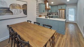 A dining area with a wooden table and chairs, a kitchen with blue cabinets and a stainless steel refrigerator, and a patterned backsplash. - Stunning, Newly Renovated Villa! Close to Strip #2 (Pigeon Forge)