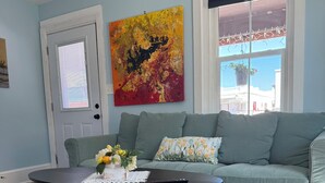 Uma sala de estar com um sofá cinzento, uma mesa de centro preta com um manete de renda e uma pintura abstrata colorida na parede.