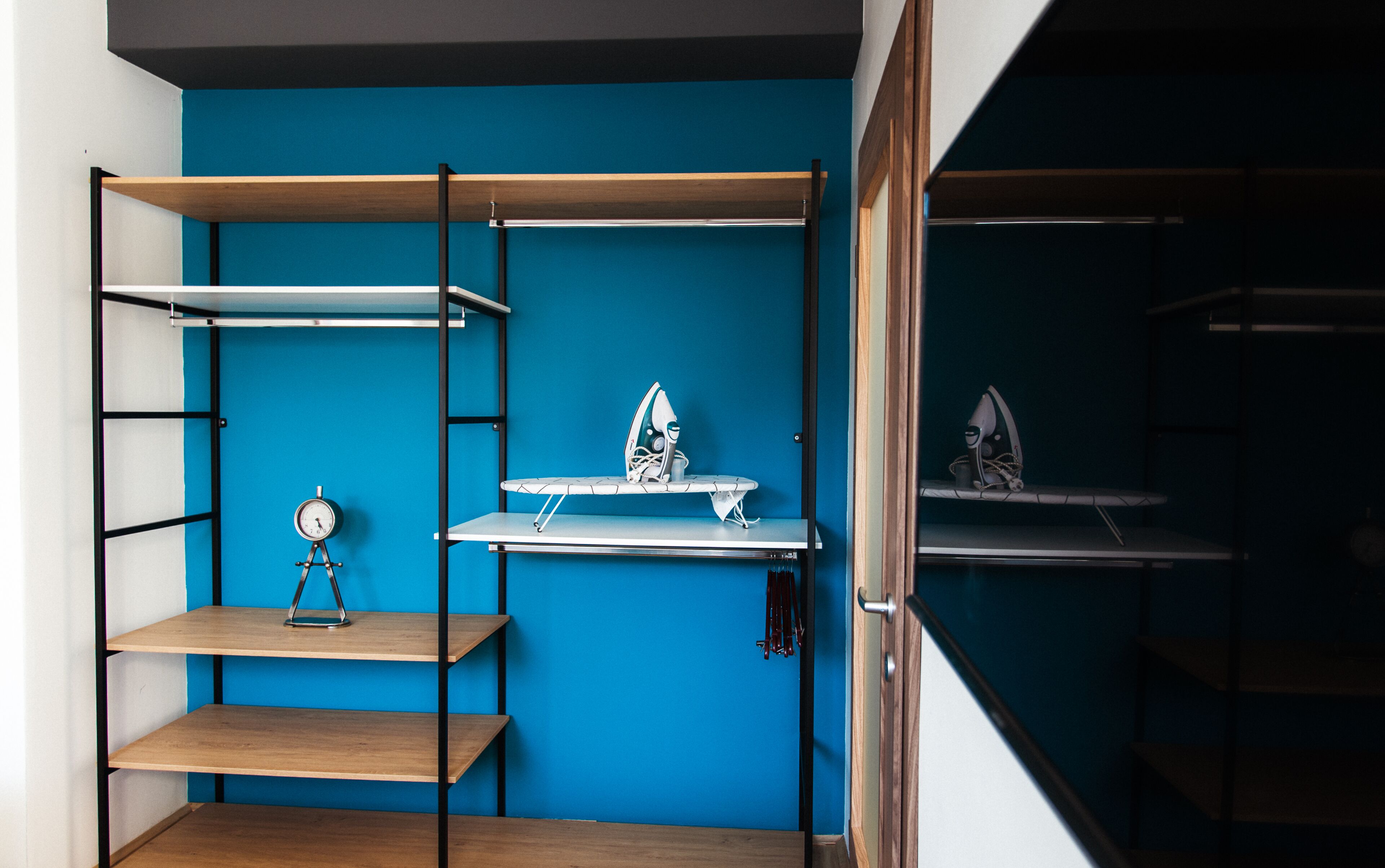 Una habitación con pared azul, estanterías de madera y una tabla de planchar.