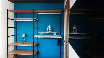 Una habitación con pared azul, estanterías de madera y una tabla de planchar.