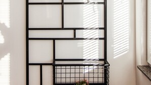 Een wandplank van zwart metaal met een geometrisch patroon, waarop een potplant en decoratieve stenen staan.