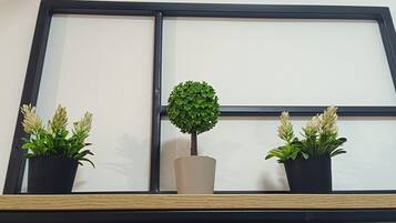 A window with a black frame and a shelf below it. On the shelf, there are three potted plants, one in a black pot and two in beige pots.