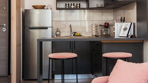 Een moderne keuken met donkere kastjes, een roestvrijstalen koelkast, een barkruk en een roze bank.