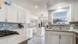 Una cocina moderna con armarios blancos, encimera de mármol y un amplio ventanal.