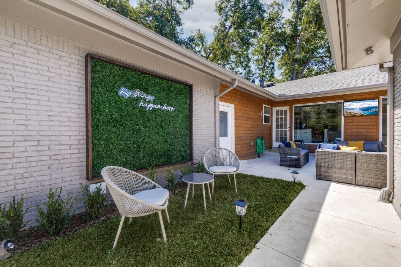 A modern outdoor patio with a green wall, wicker furniture, and a clear view of the house.