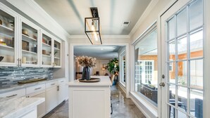 Una cocina amplia con muebles blancos, una isla central y vistas al exterior a través de grandes ventanales.