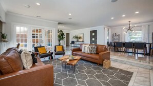 Un salón espacioso con un sofá de cuero marrón, dos sillones, una mesa de centro y una zona de comedor con mesa y sillas.