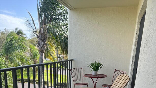 A wooden deck with two Adirondack chairs, a small round table, and a potted plant.
