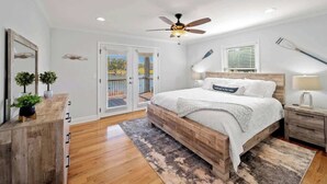 A bedroom with a wooden bed, a ceiling fan, a nightstand, a lamp, and a view of the outdoors through a sliding glass door. - Lakefront Home w/Hot Tub, Fire Pit & Boat Slip (Eatonton)