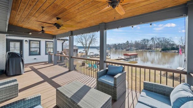 A covered deck with wicker furniture, a view of a lake, and a barbecue grill. - Lakefront Home w/Hot Tub, Fire Pit & Boat Slip (Eatonton)