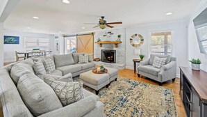 A spacious living room with a large sectional sofa, a fireplace, and a ceiling fan. - Lakefront Home w/Hot Tub, Fire Pit & Boat Slip (Eatonton)