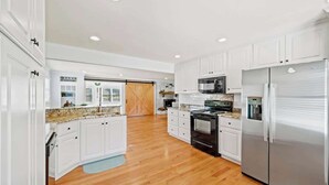 A spacious kitchen with white cabinets, a stainless steel refrigerator, a microwave, and a stove. - Lakefront Home w/Hot Tub, Fire Pit & Boat Slip (Eatonton)