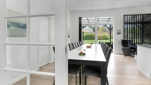 Un comedor moderno con una mesa larga, sillas negras y vistas a un jardín a través de amplios ventanales.