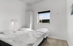 Un dormitori minimalista amb un llit, una làmpada de nit i una finestra que mostra un edifici.