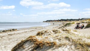 Una playa con arena, dunas y una línea costera distante con edificios.