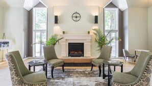 A living room with a fireplace, two armchairs, a coffee table, and a side table. There are two large windows and a clock on the wall. - ROMANTIC SPA RETREAT MINUTES TO MOHEGAN SUN CASINO (Norwich)