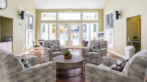 A spacious lobby with a central round table, two armchairs, and a sofa. There are large windows with a view of a pool and greenery. - ROMANTIC SPA RETREAT MINUTES TO MOHEGAN SUN CASINO (Norwich)