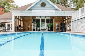 A swimming pool with a wooden deck and a covered area with chairs and tables.