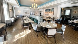 Un restaurante espacioso con techos altos, un área central de asientos con un banco acolchado y numerosas mesas de comedor.