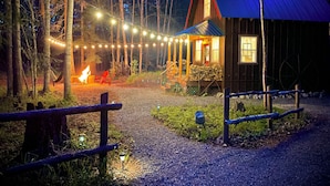 Eine Hütte mit Veranda, Lichterkette, Feuerstelle und Kiesweg.