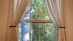 Ein Fenster mit durchscheinenden Vorhängen, Holzrahmen und Blick auf einen Wald.