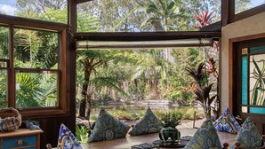 A dining area with a view of a garden and pond, wooden furniture, and patterned cushions.